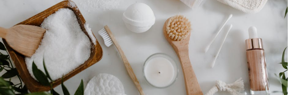 Flat lay of natural spa essentials including salts, soap, brush, and greenery.